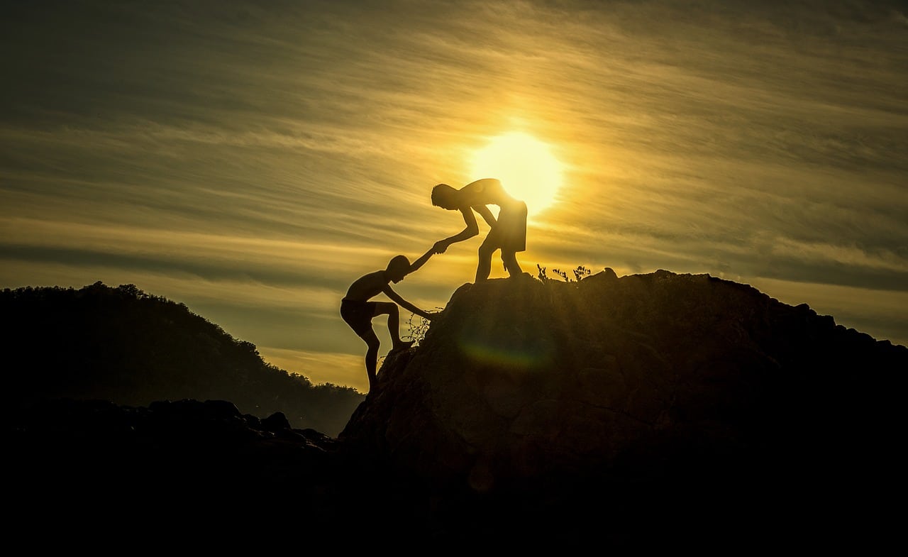 Two people helping each other up a mountain