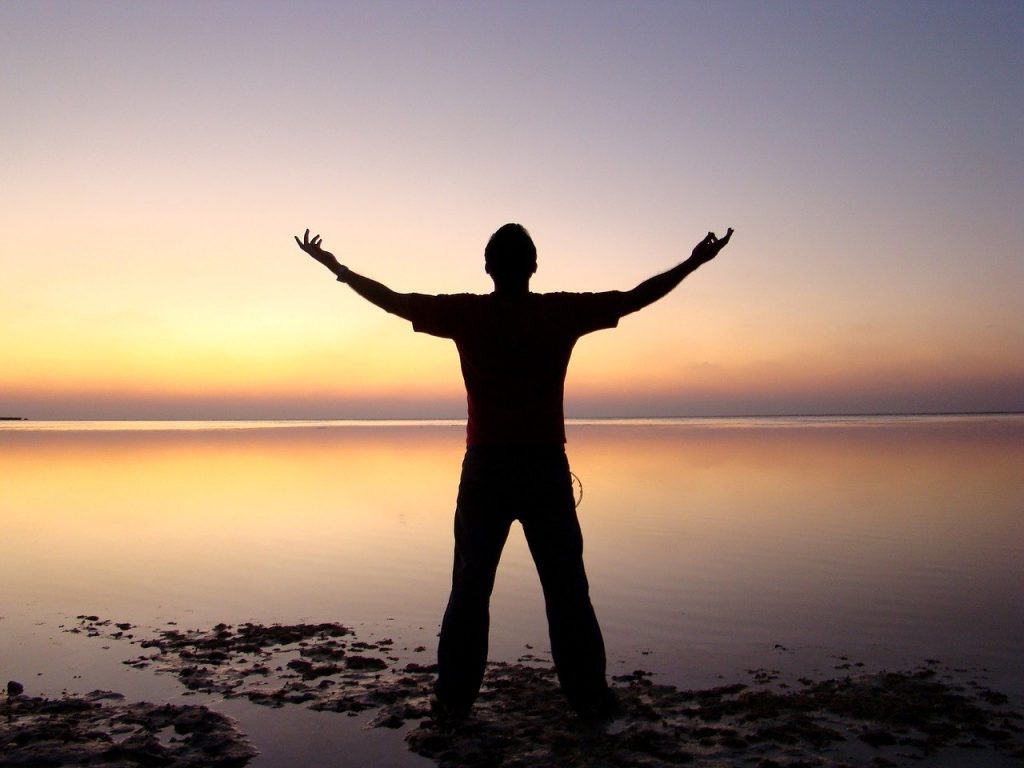 Man holding his hands up in front of clear sea and sunset