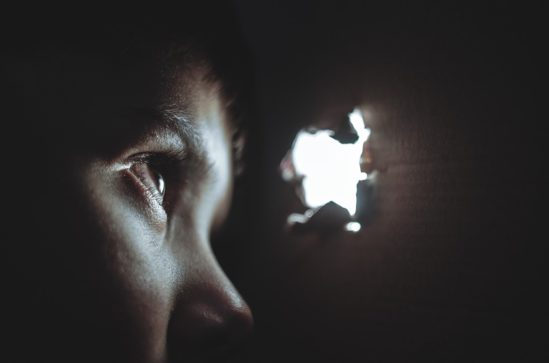 Boy peering through a hole looking afraid