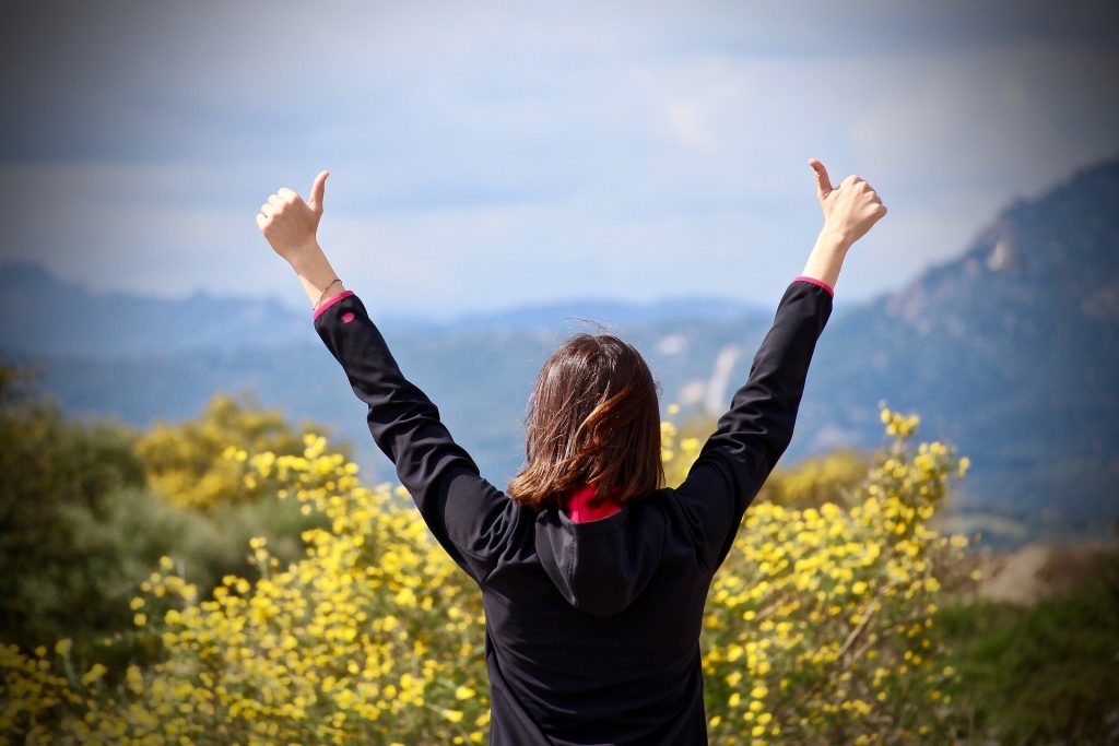 confident woman holding arms up in air with thumbs up
