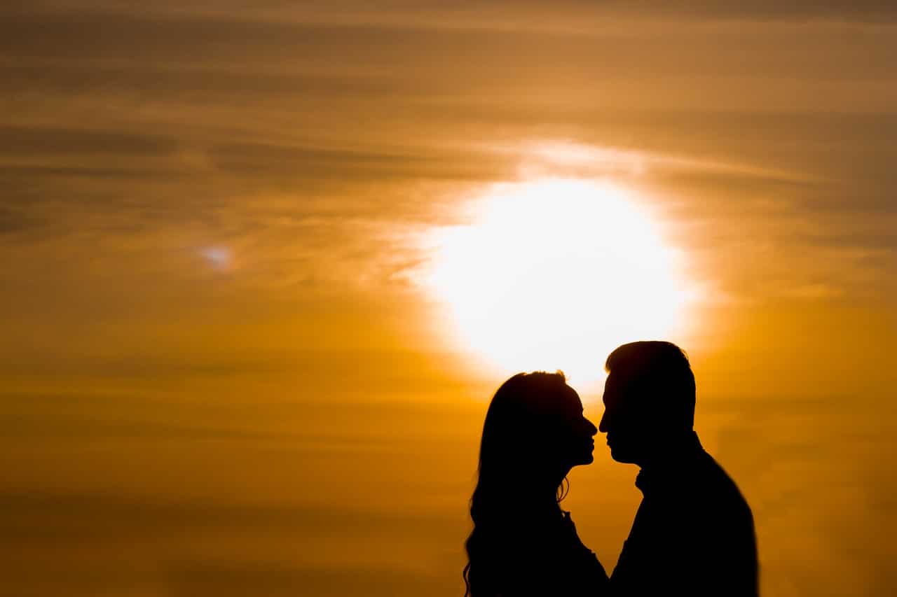 man and woman kissing with the sun behind them