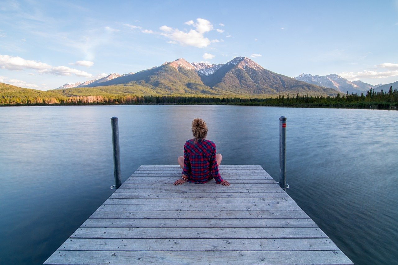 Woman sat on a jetty in front of a lake adopting the simple habit of mindfulness to help improve mental health