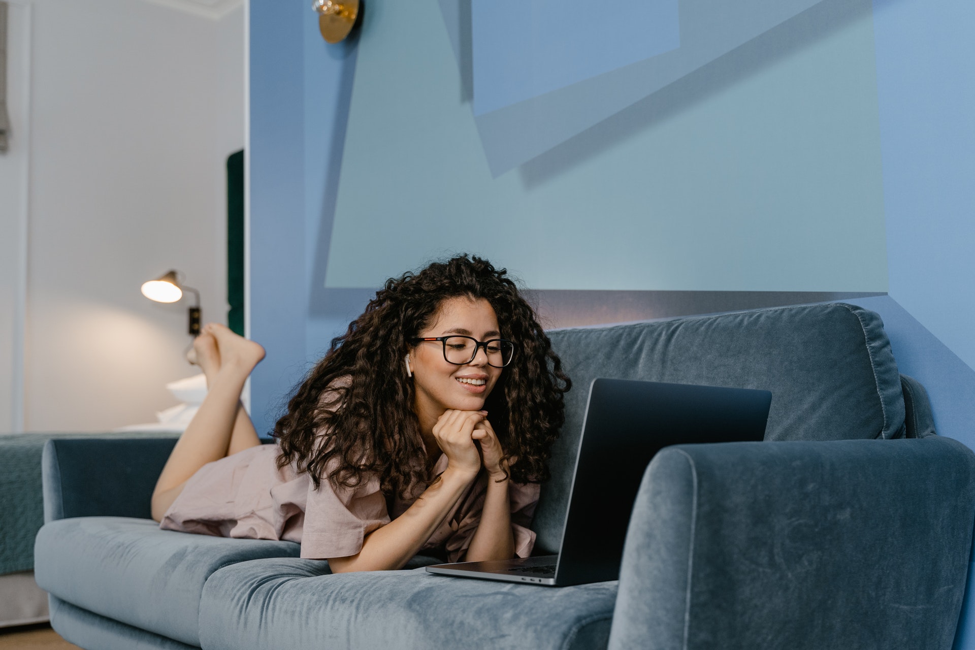 woman lying on a sofa smiling while watching mental wellbeing videos - mental wellbeing videos