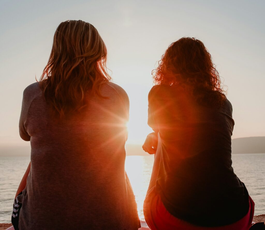 Two people sat with next to the sea with the sun in front of them - intro to How to Support a Friend Struggling with Their Mental Health Intro