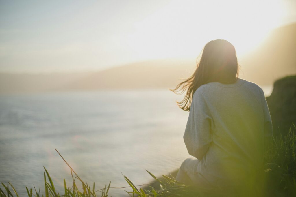 Woman wearing long sleeved grey t-shirt facing the sea - How to embrace slow living